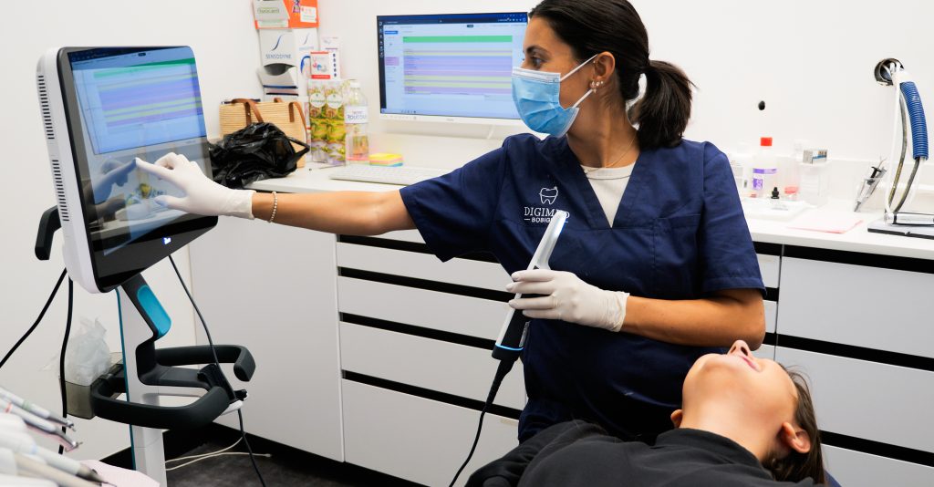 Praticien consultant les données numériques sur un écran tactile tout en tenant un scanner intra-oral.