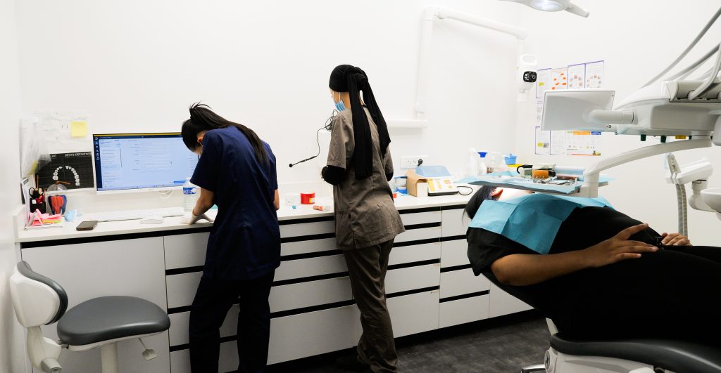 Vue générale d'une salle de soins moderne avec poste informatique et fauteuil dentaire équipé.